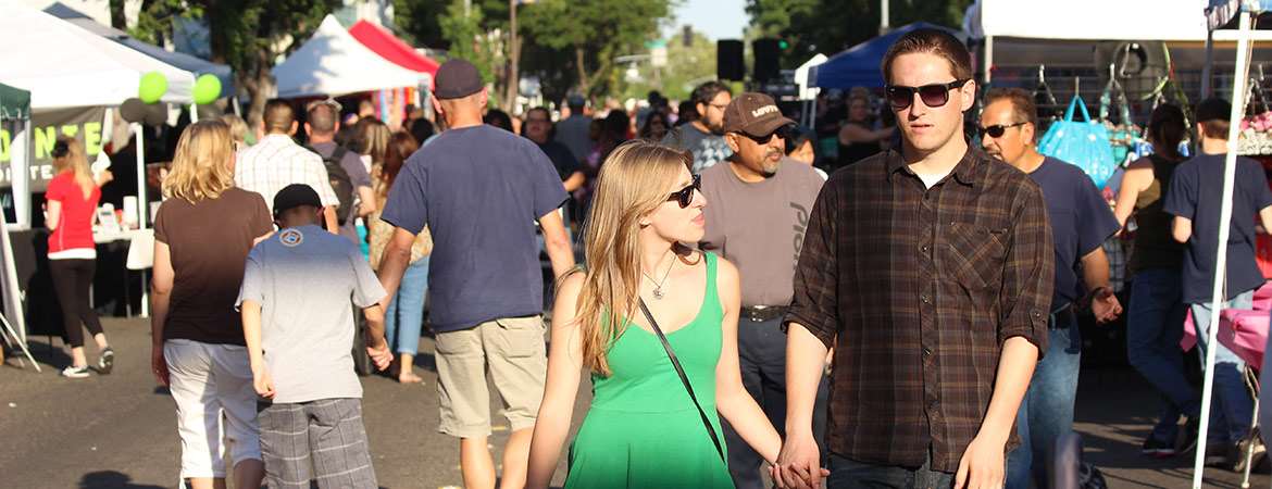 Several dozen people enjoy an outdoor street fair in downtown Merced.